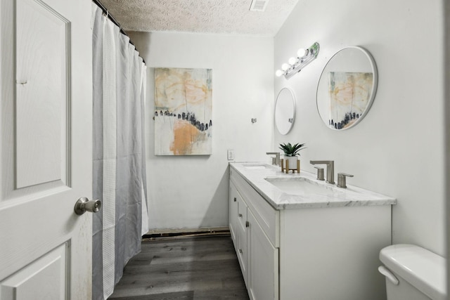 bathroom featuring a textured ceiling, wood finished floors, toilet, and a sink
