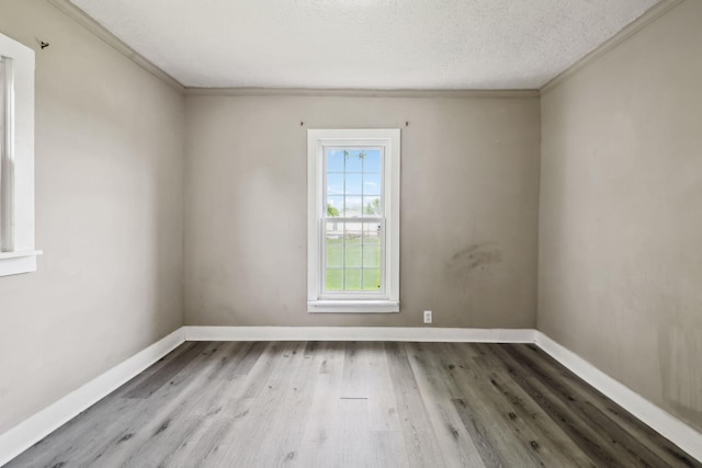 empty room with wood finished floors, baseboards, and ornamental molding