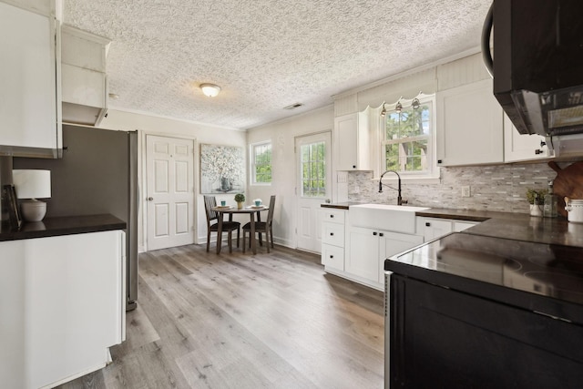 kitchen featuring a sink, black range with electric stovetop, ventilation hood, backsplash, and dark countertops