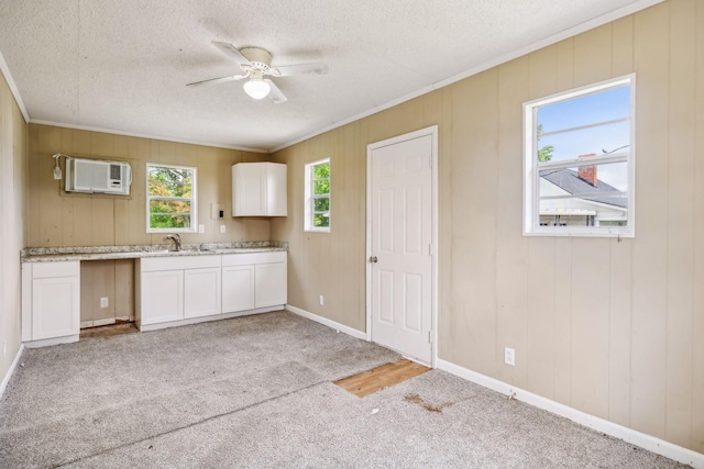 kitchen with a ceiling fan, a wall unit AC, ornamental molding, a sink, and white cabinetry