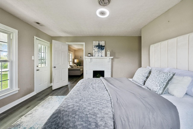 bedroom featuring wood finished floors, visible vents, baseboards, and a brick fireplace