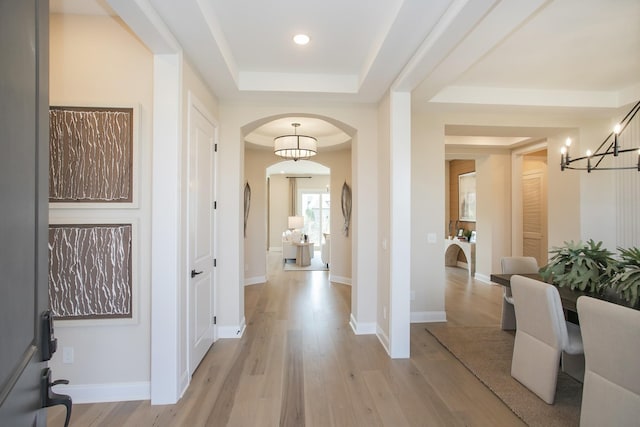 foyer entrance with light wood finished floors, an inviting chandelier, a raised ceiling, arched walkways, and recessed lighting
