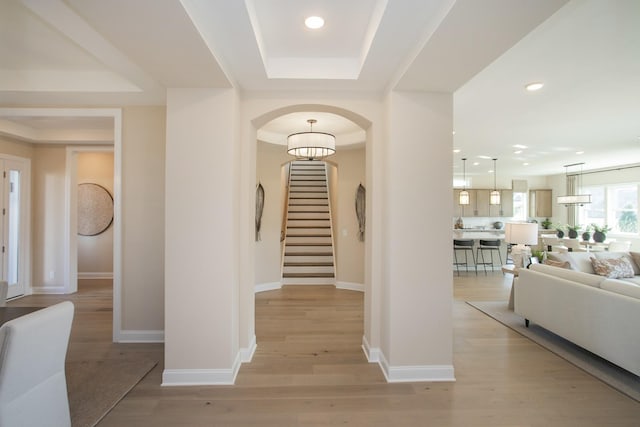 foyer entrance with light wood finished floors, a tray ceiling, stairway, baseboards, and arched walkways