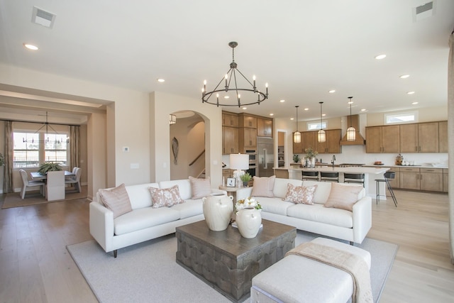 living area featuring a chandelier, plenty of natural light, visible vents, and arched walkways
