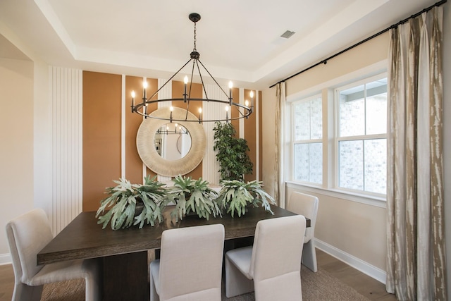 dining room with a notable chandelier, a tray ceiling, baseboards, visible vents, and wood finished floors