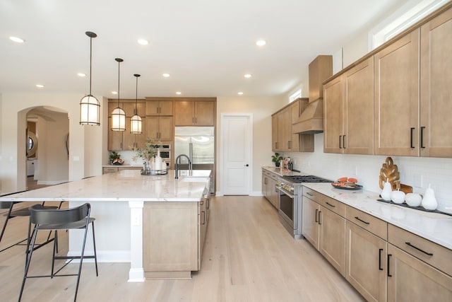 kitchen with a sink, decorative backsplash, high quality appliances, arched walkways, and light wood-type flooring