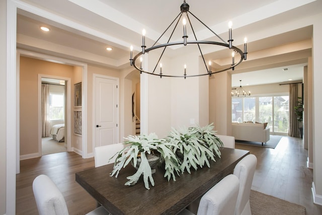 dining space with a tray ceiling, a chandelier, arched walkways, and wood finished floors