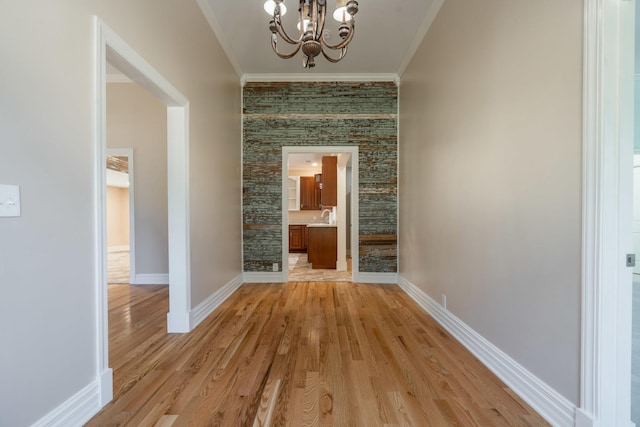 hallway with a chandelier, crown molding, baseboards, and light wood-style floors