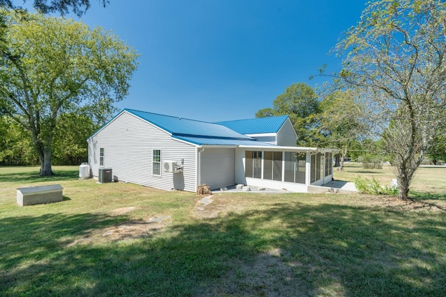 back of house with central AC unit, metal roof, a sunroom, and a lawn