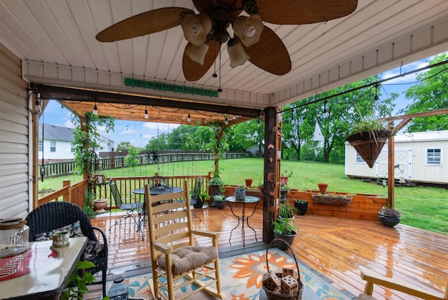 wooden deck featuring fence, an outdoor structure, a shed, a ceiling fan, and a lawn