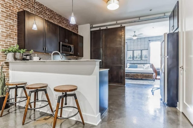 210 30th Ave N Unit 207, Nashville, TN 37203 - kitchen featuring dark brown cabinets, brick wall, ceiling fan, finished concrete floors, and appliances with stainless steel finishes