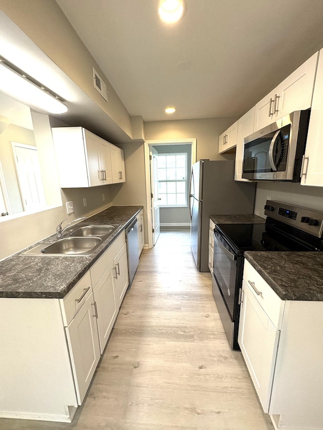 kitchen featuring stainless steel appliances, a sink, white cabinets, light wood finished floors, and recessed lighting