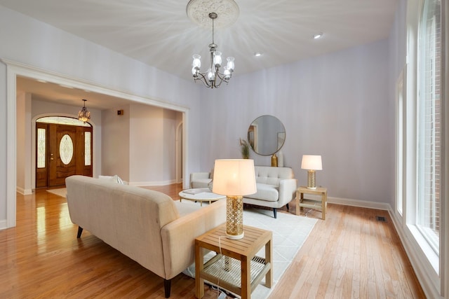 living room with light wood finished floors, a wealth of natural light, a chandelier, and baseboards