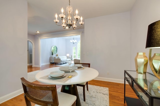 dining area with arched walkways, baseboards, an inviting chandelier, and light wood-type flooring