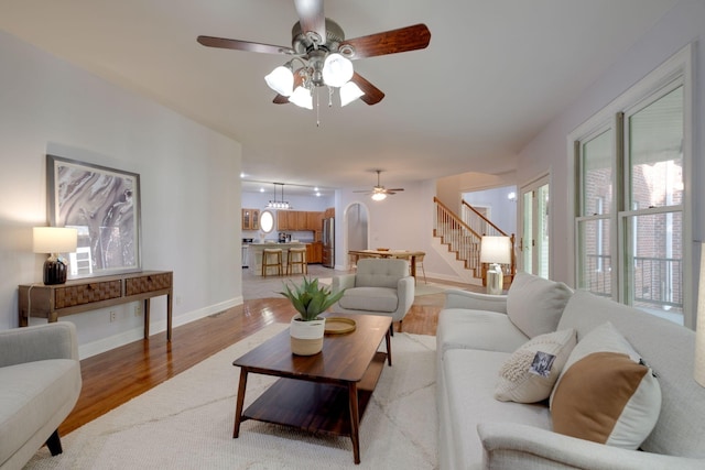 living area featuring stairway, light wood finished floors, baseboards, and a ceiling fan