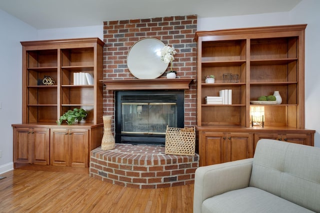 living area with light wood finished floors, a brick fireplace, and baseboards