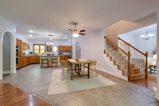 dining area with arched walkways, stairway, baseboards, and ceiling fan with notable chandelier