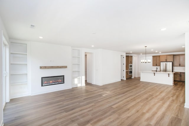 126 W Cassa Way, Mount Juliet, TN 37122 - unfurnished living room with a notable chandelier, light wood-style flooring, recessed lighting, a glass covered fireplace, and built in features