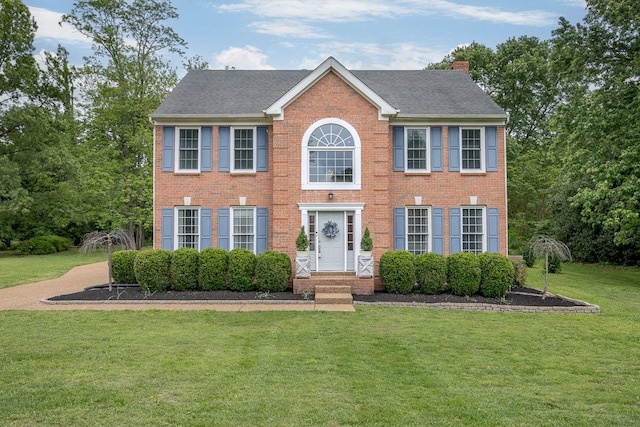 colonial-style house with a front lawn, a shingled roof, brick siding, and a chimney