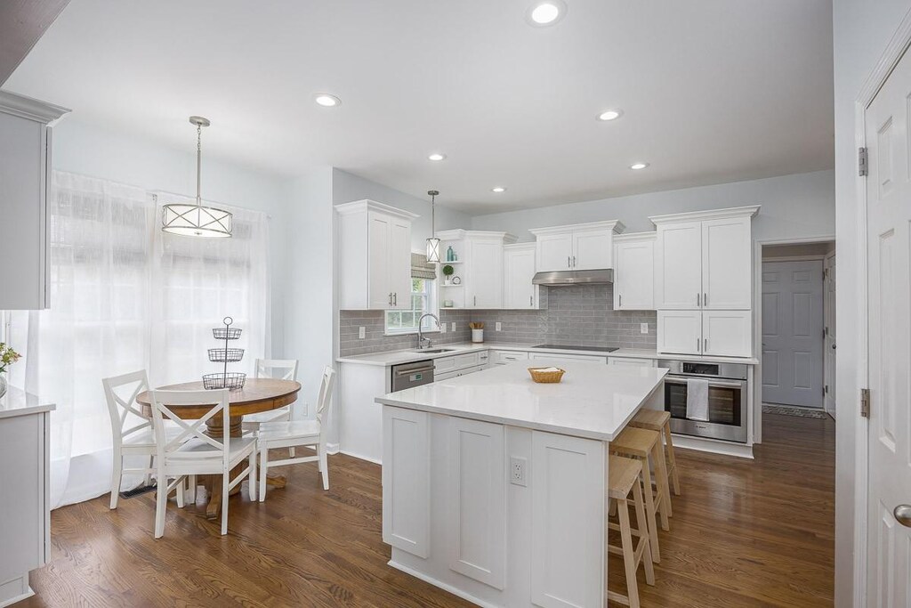 kitchen featuring under cabinet range hood, light countertops, dark wood-style floors, white cabinets, and appliances with stainless steel finishes