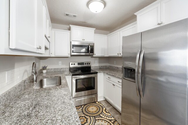 kitchen with light stone counters, visible vents, a sink, white cabinets, and appliances with stainless steel finishes