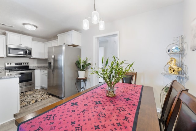 kitchen with stainless steel appliances, light wood-type flooring, visible vents, white cabinets, and light stone countertops