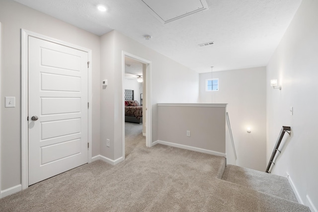 carpeted empty room featuring baseboards, visible vents, and attic access