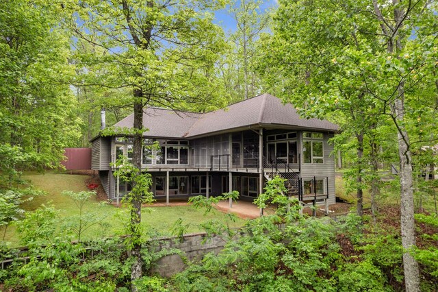 rear view of property featuring a patio, a sunroom, a deck, a shingled roof, and stairway