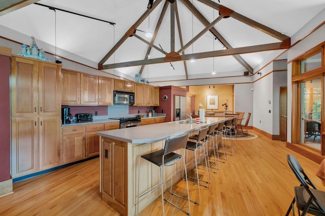 kitchen featuring high vaulted ceiling, a sink, appliances with stainless steel finishes, baseboards, and light wood-style floors