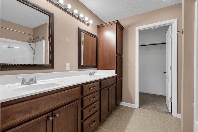 full bathroom with tile patterned floors, double vanity, a sink, and a walk in closet