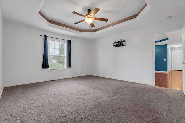 carpeted empty room with a tray ceiling, ornamental molding, baseboards, and a ceiling fan