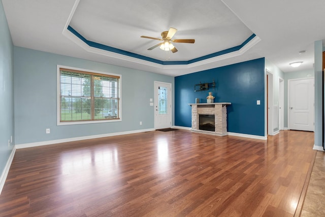 unfurnished living room with wood finished floors, a fireplace, a ceiling fan, a raised ceiling, and baseboards