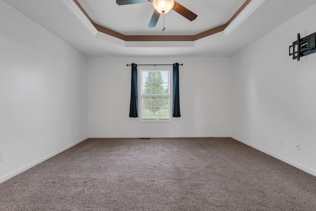 spare room with ornamental molding, carpet floors, a ceiling fan, a tray ceiling, and baseboards