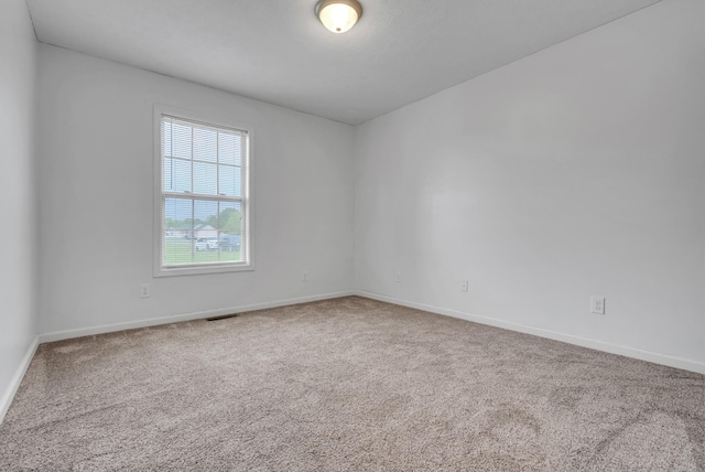empty room with carpet, visible vents, and baseboards
