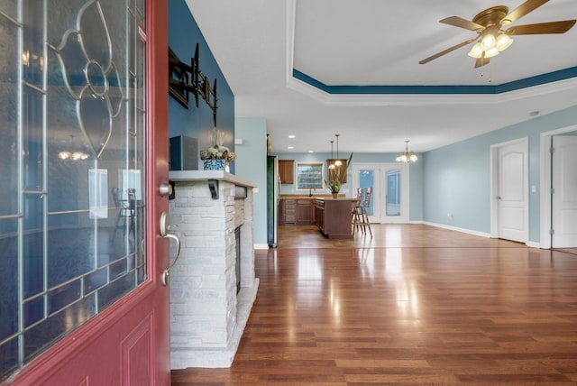 foyer featuring a fireplace, baseboards, a raised ceiling, dark wood-style flooring, and ceiling fan