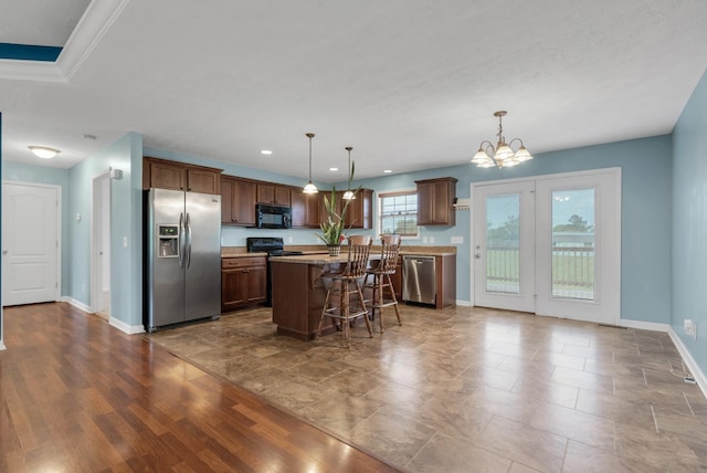 kitchen featuring a breakfast bar, black appliances, a kitchen island, hanging light fixtures, and baseboards