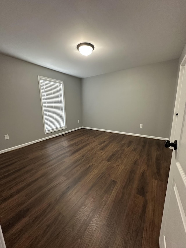 unfurnished room with baseboards and dark wood-type flooring