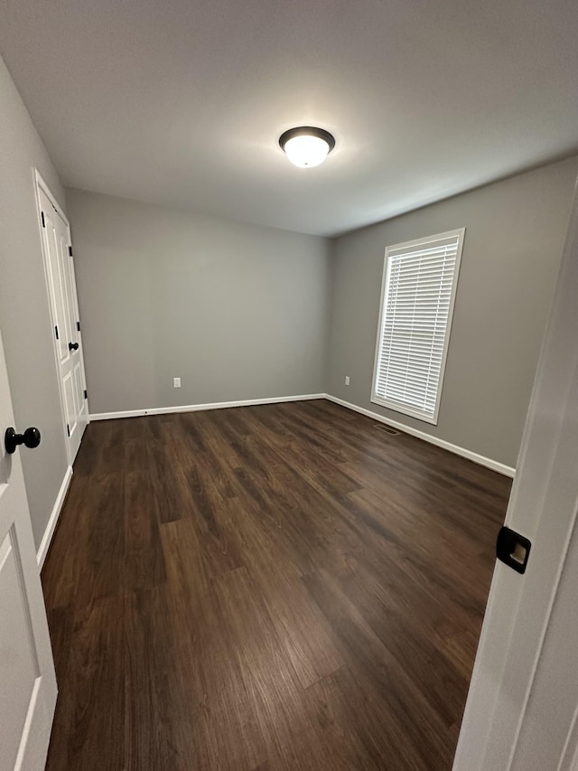 spare room featuring baseboards and dark wood finished floors