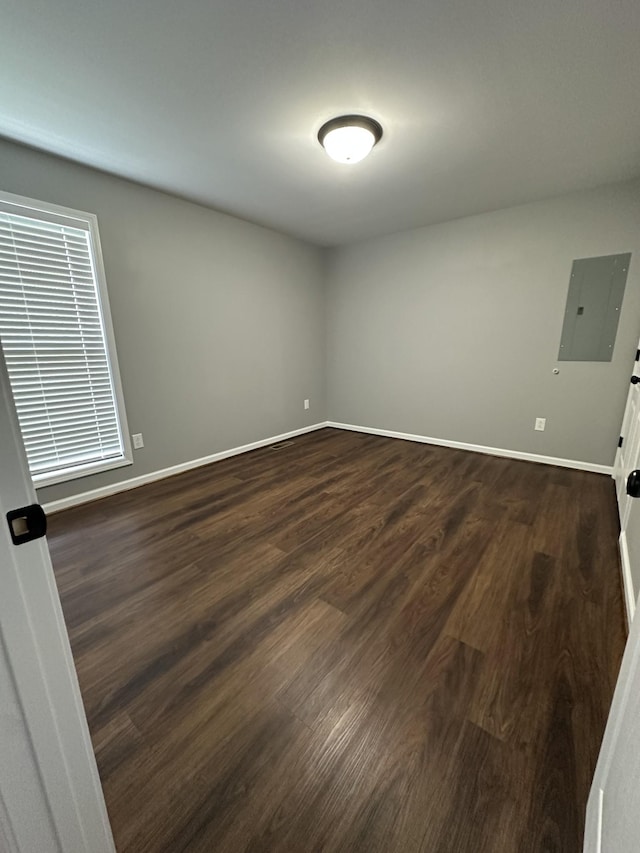 unfurnished room with electric panel, baseboards, and dark wood-style floors