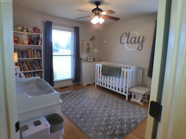 bedroom featuring ceiling fan, a crib, and wood finished floors