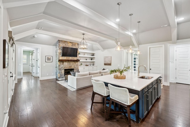kitchen featuring a stone fireplace, a sink, lofted ceiling with beams, light countertops, and dark wood-style floors
