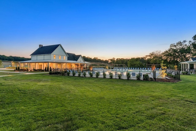 back of property at dusk featuring fence, a fenced in pool, a chimney, and a lawn
