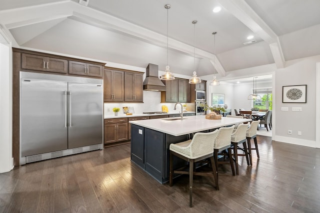 kitchen with built in appliances, custom range hood, lofted ceiling with beams, light countertops, and an island with sink