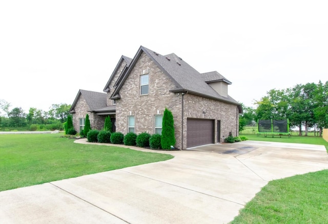 view of side of home with a yard, a trampoline, concrete driveway, brick siding, and roof with shingles