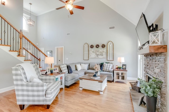 living area with ceiling fan with notable chandelier, ornamental molding, high vaulted ceiling, visible vents, and a stone fireplace