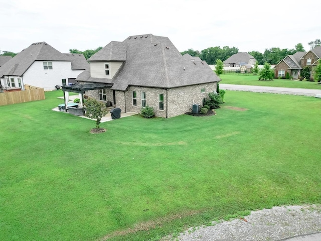 rear view of house with a yard, a patio area, stone siding, and fence
