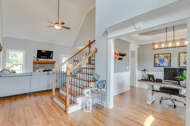 stairs with ceiling fan, crown molding, wood finished floors, and a stone fireplace