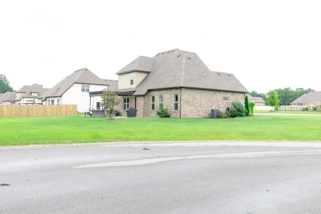 exterior space featuring central AC unit, fence, brick siding, and a lawn