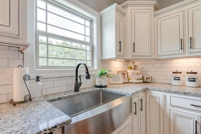 kitchen with backsplash, light stone counters, and a sink