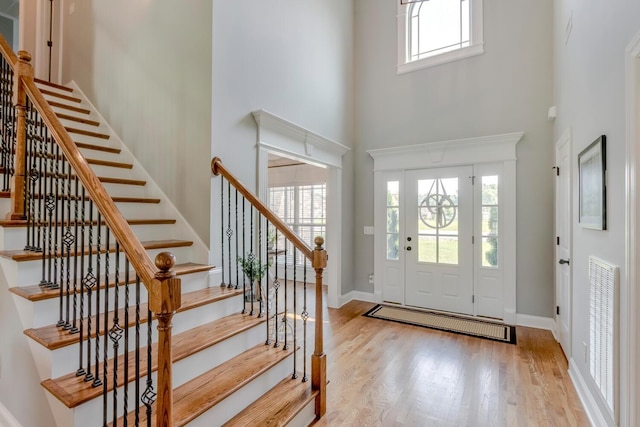 foyer entrance with light wood-style flooring, baseboards, a high ceiling, and stairs